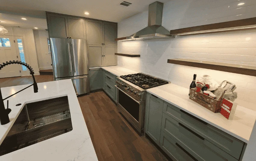 Kitchen with muted green cabinetry, bright walls and wooden shelves.